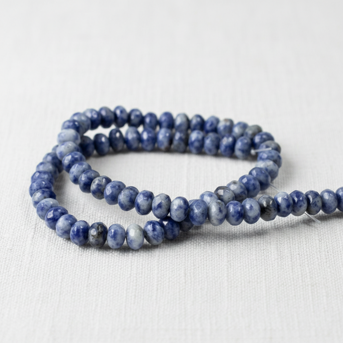Hackberry Creek faceted denim lapis rondelle beads in blue and gray on a white fabric background
