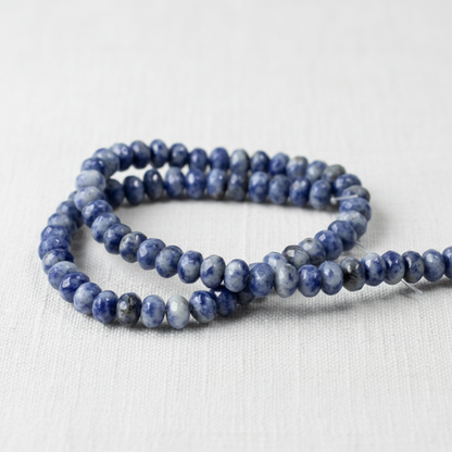 Hackberry Creek faceted denim lapis rondelle beads in blue and gray on a white fabric background