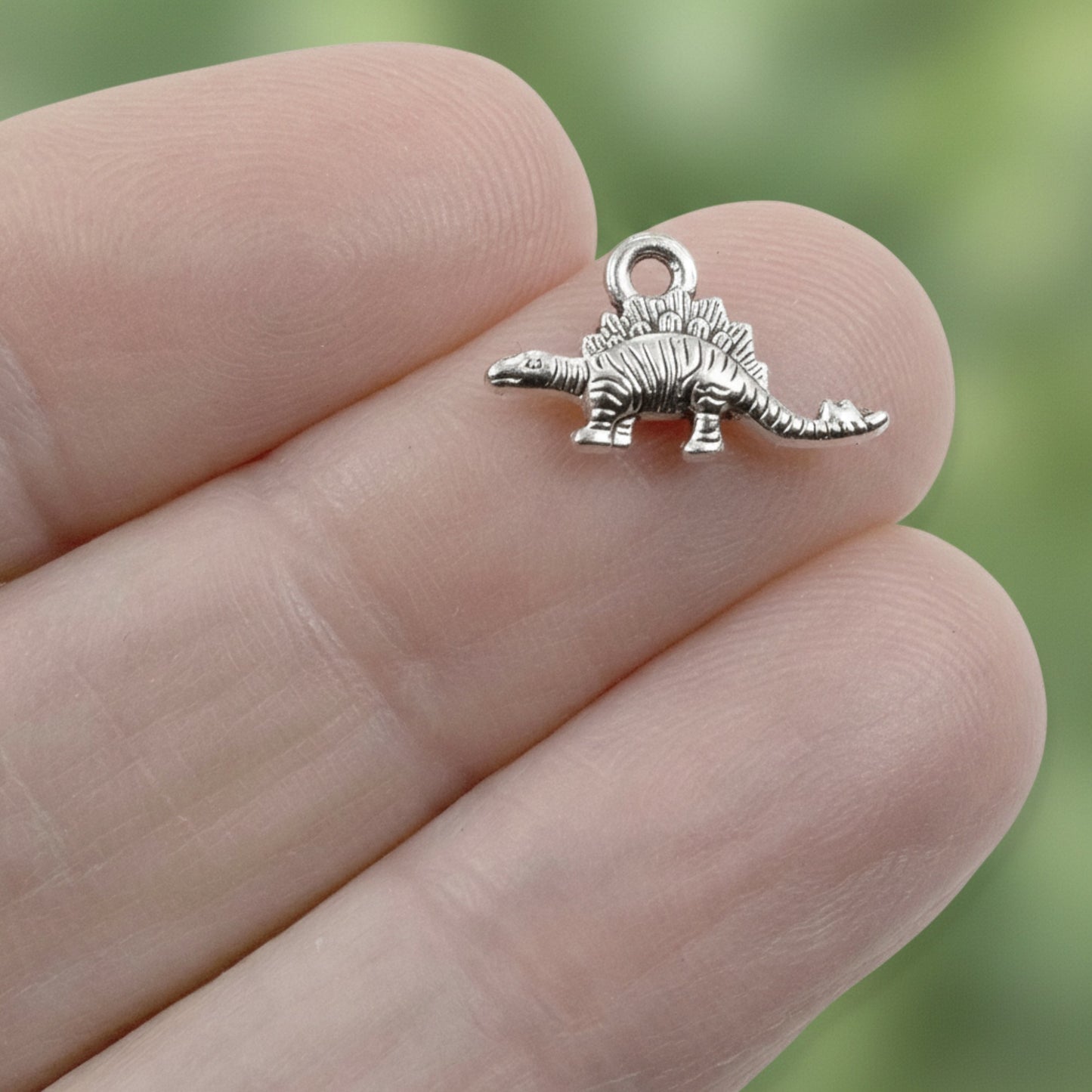 Hackberry Creek tiny antique silver dinosaur charm held between fingers for scale, showing detailed metal texture.