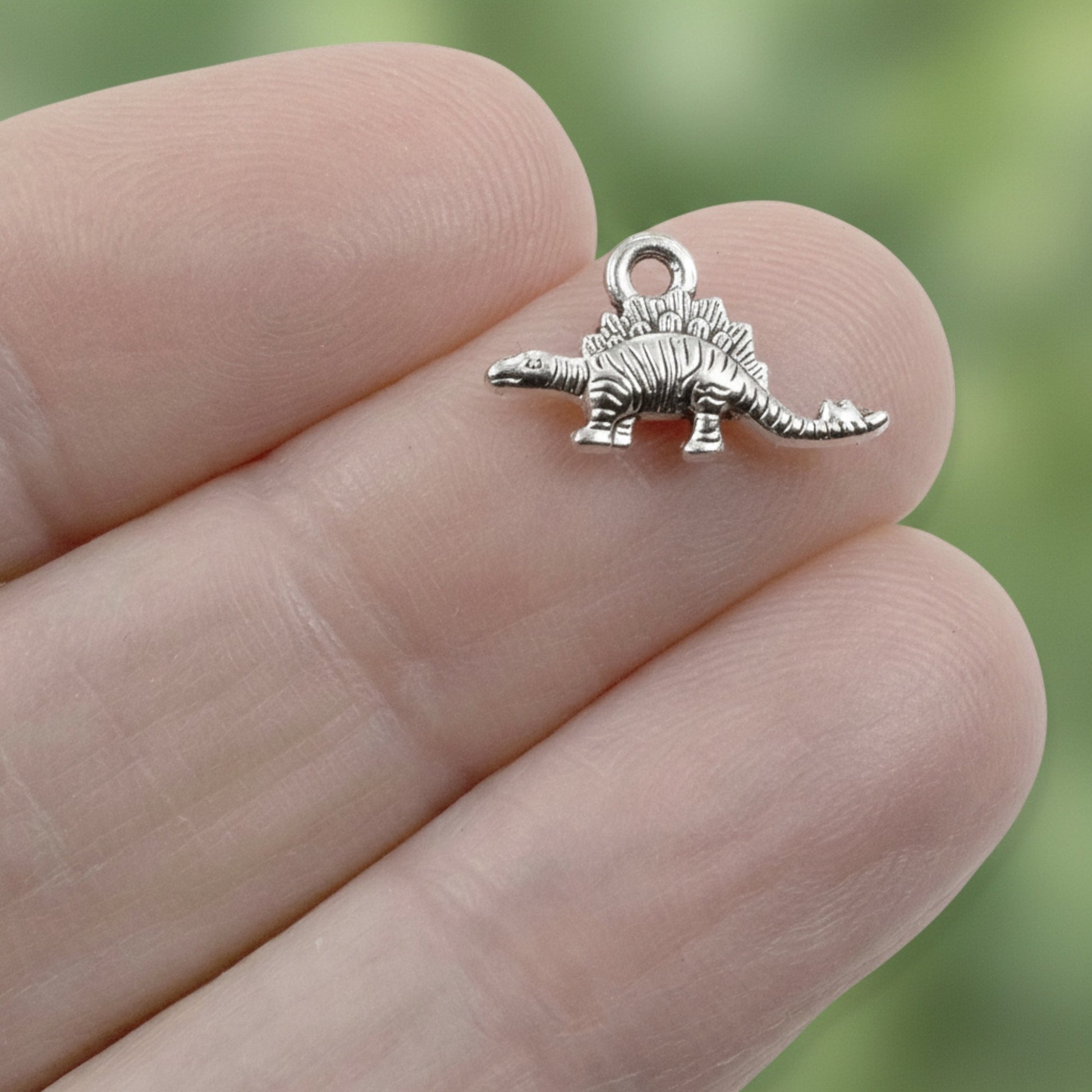 Hackberry Creek tiny antique silver dinosaur charm held between fingers for scale, showing detailed metal texture.