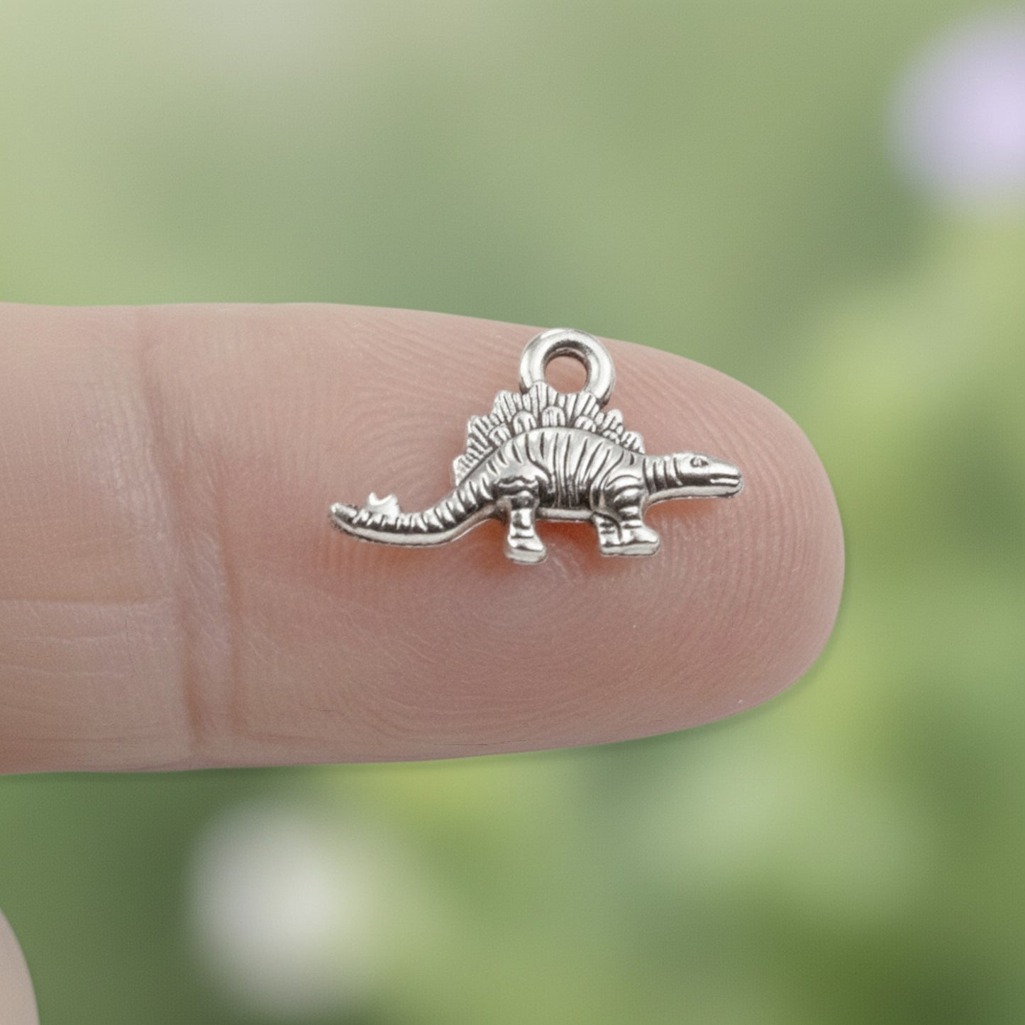 Hackberry Creek antique silver metal dinosaur charm held on a fingertip for scale