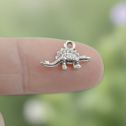 Hackberry Creek antique silver metal dinosaur charm held on a fingertip for scale
