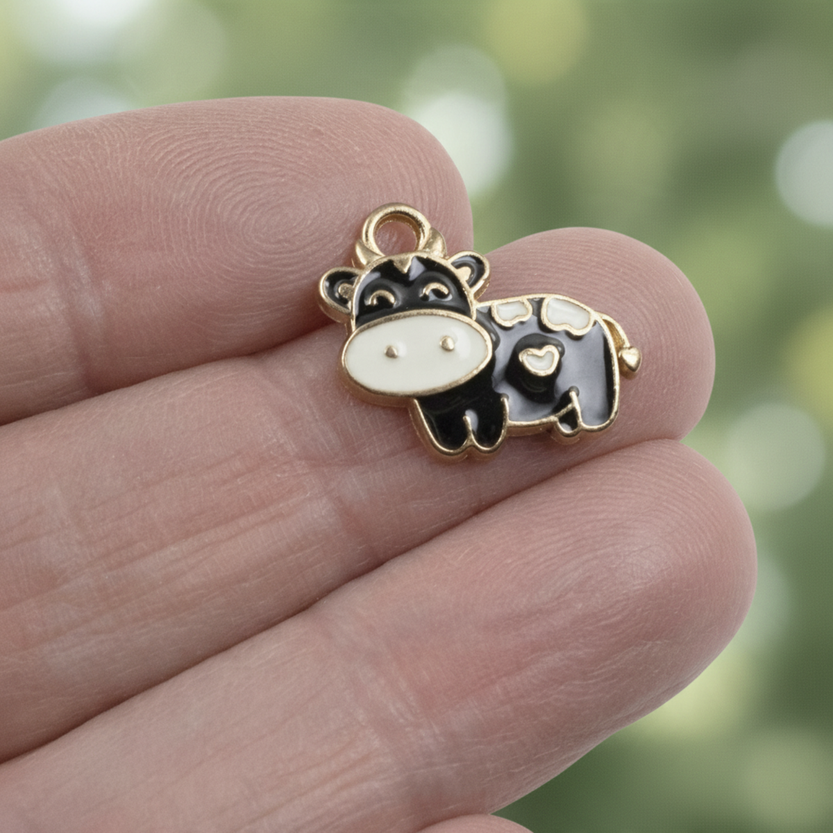 Hackberry Creek black and ivory enamel cow charm held between fingers for farmhouse jewelry making