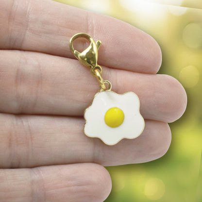 Hackberry Creek enamel egg charm with a yellow yolk and gold-plated lobster clasp held in a hand