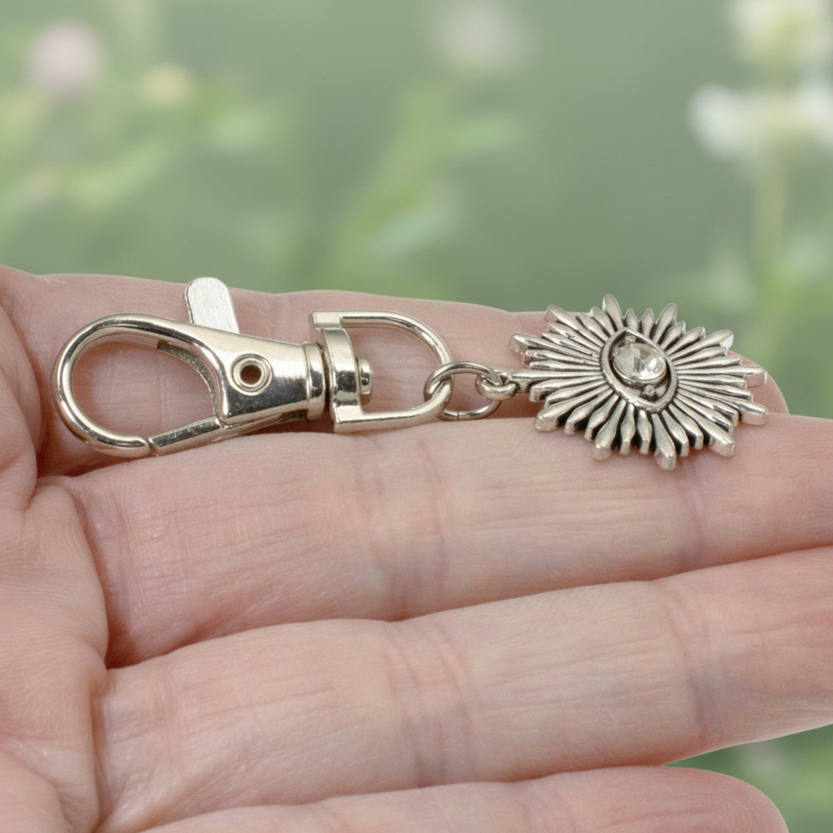 Hackberry Creek silver metal alloy evil eye sunburst bag charm with a clear rhinestone accent held in a hand