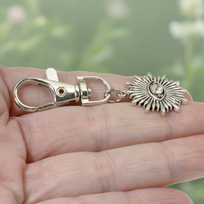 Hackberry Creek silver metal alloy evil eye sunburst bag charm with a clear rhinestone accent held in a hand