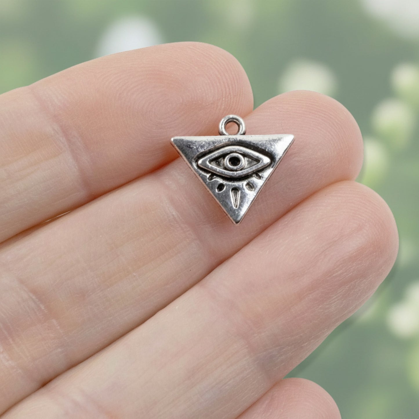 Hackberry Creek antique silver triangle charm with a recessed evil eye motif held between fingers