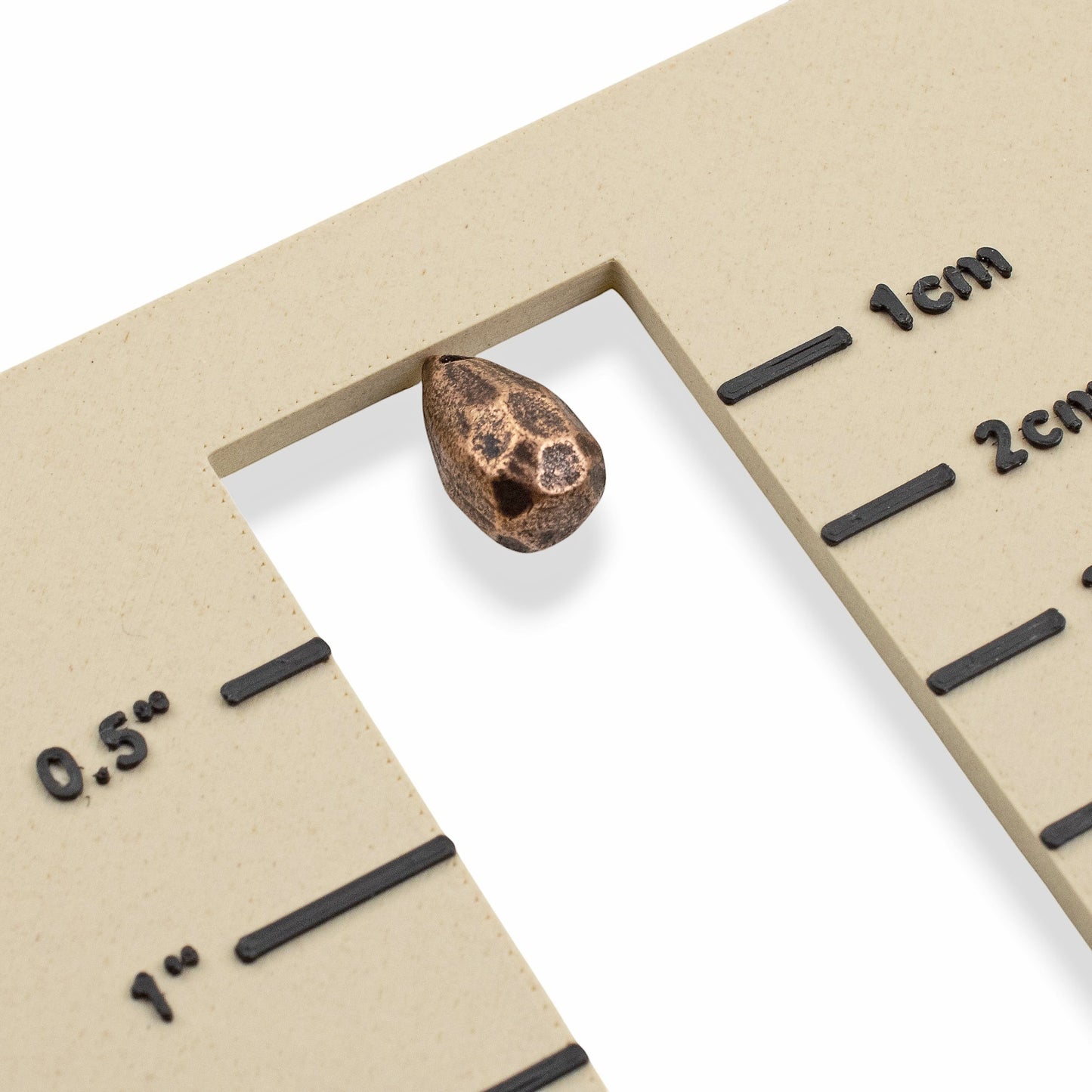 Hackberry Creek faceted drop bead in antique copper-plated pewter shown against a measurement gauge for scale.