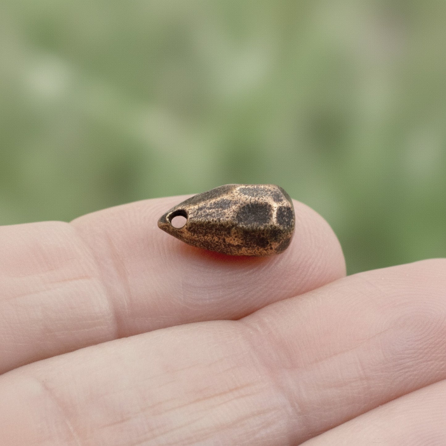 Hackberry Creek faceted drop bead in antique copper-plated pewter held on a finger for scale.