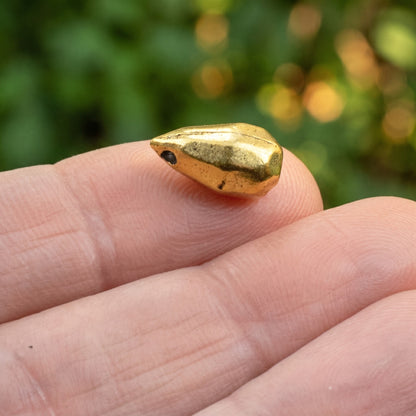 Hackberry Creek faceted drop bead made of antique 24K gold-plated pewter held on a fingertip