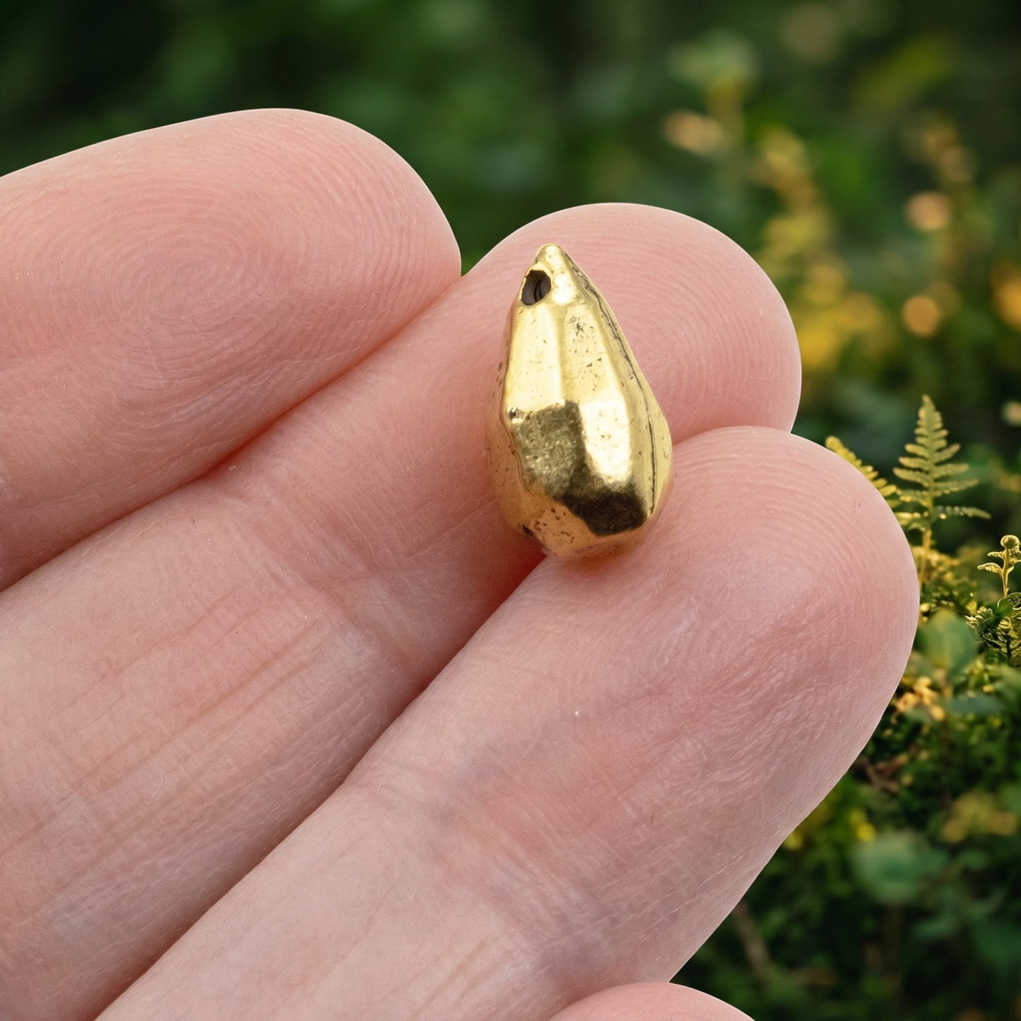 Hackberry Creek faceted drop bead made of 24K gold-plated pewter with an antique finish held between fingers.