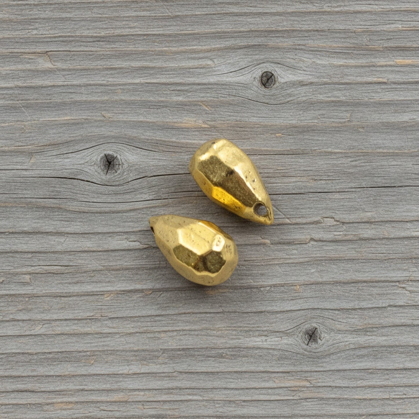 Hackberry Creek faceted antique 24K gold-plated pewter teardrop beads for jewelry making on a rustic wood background