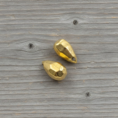 Hackberry Creek faceted antique 24K gold-plated pewter teardrop beads for jewelry making on a rustic wood background