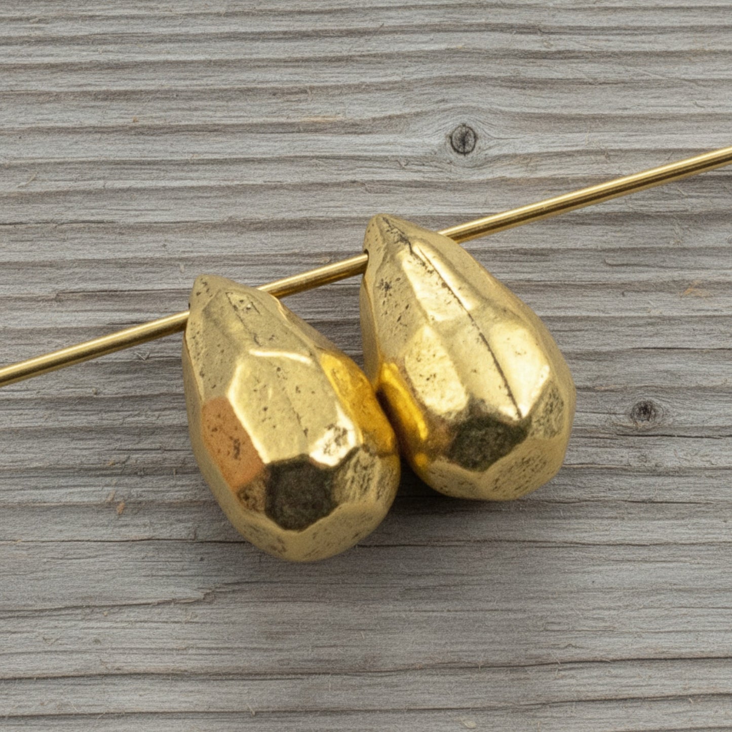 Hackberry Creek faceted antique 24K gold-plated pewter teardrop beads for jewelry making on a wooden background