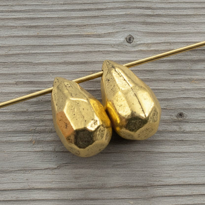 Hackberry Creek faceted antique 24K gold-plated pewter teardrop beads for jewelry making on a wooden background
