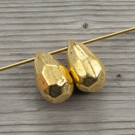 Hackberry Creek faceted antique 24K gold-plated pewter teardrop beads for jewelry making on a wooden background