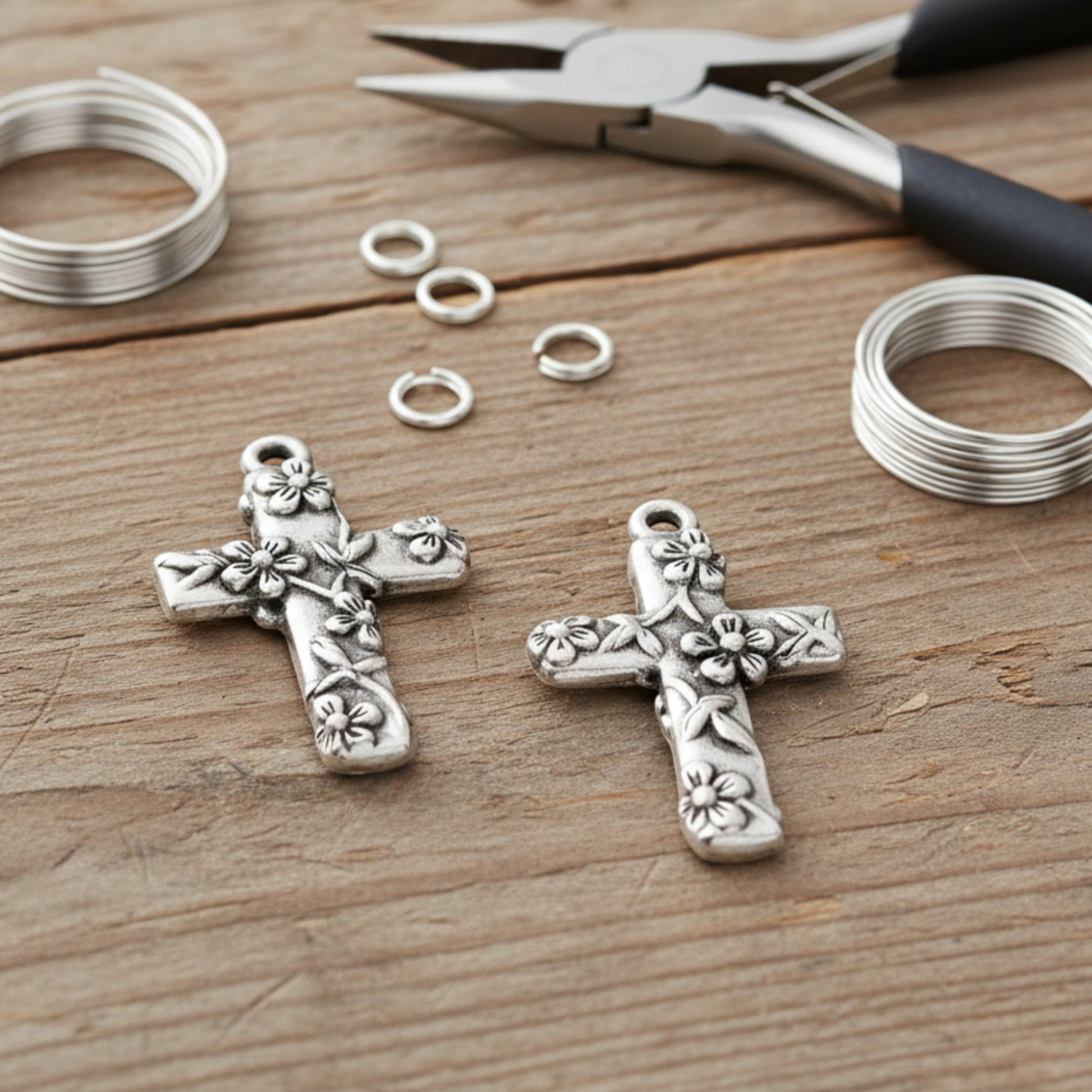 Hackberry Creek silver-plated pewter floral cross pendants with jewelry pliers and wire on a wooden surface.