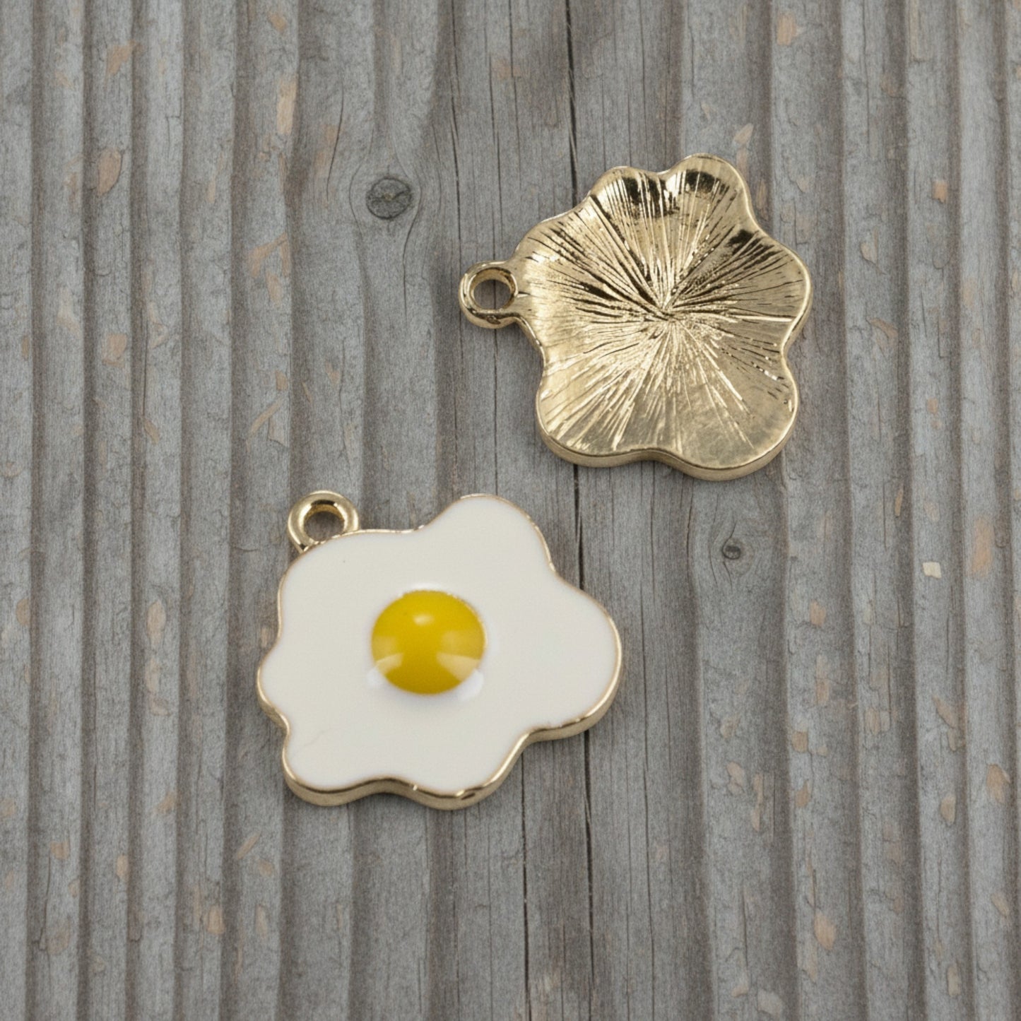 Hackberry Creek enamel fried egg charms showing the white and yellow front and textured light gold back on wood.