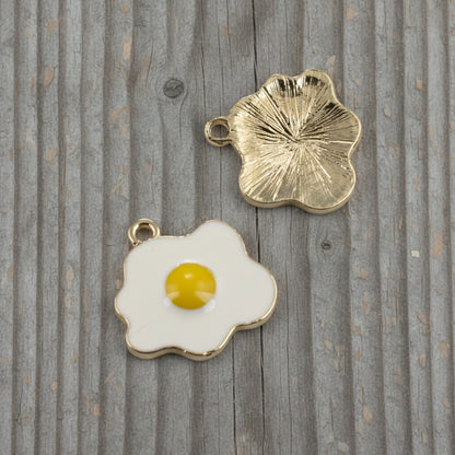 Hackberry Creek enamel fried egg charms showing the white and yellow front and textured light gold back on wood.
