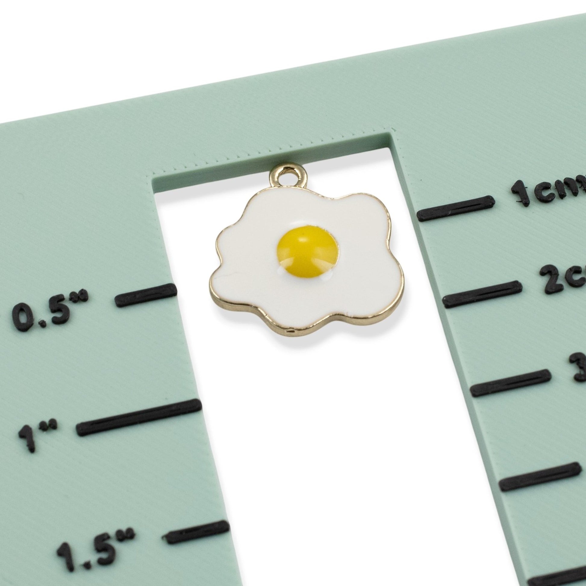 Hackberry Creek fried egg enamel charm with light gold trim on a measuring tool for jewelry making