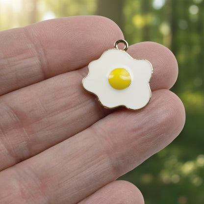 Hackberry Creek enamel fried egg charm with white and yellow finish held between fingers for jewelry making