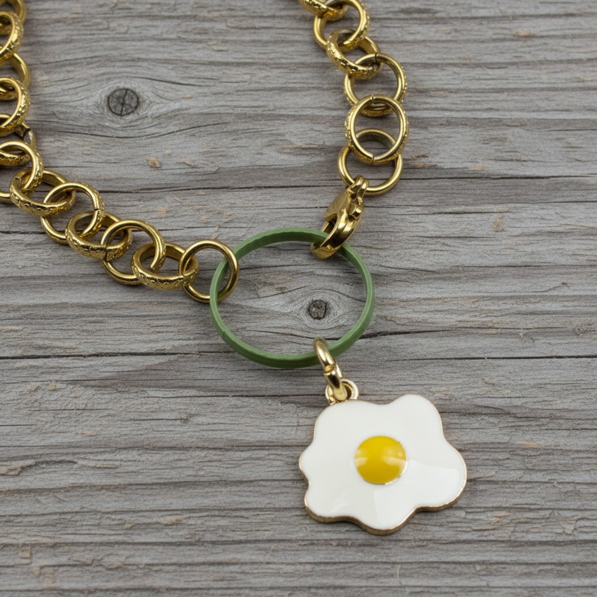 Hackberry Creek fried egg enamel charm with light gold detail hanging from a gold chain on a rustic wood background