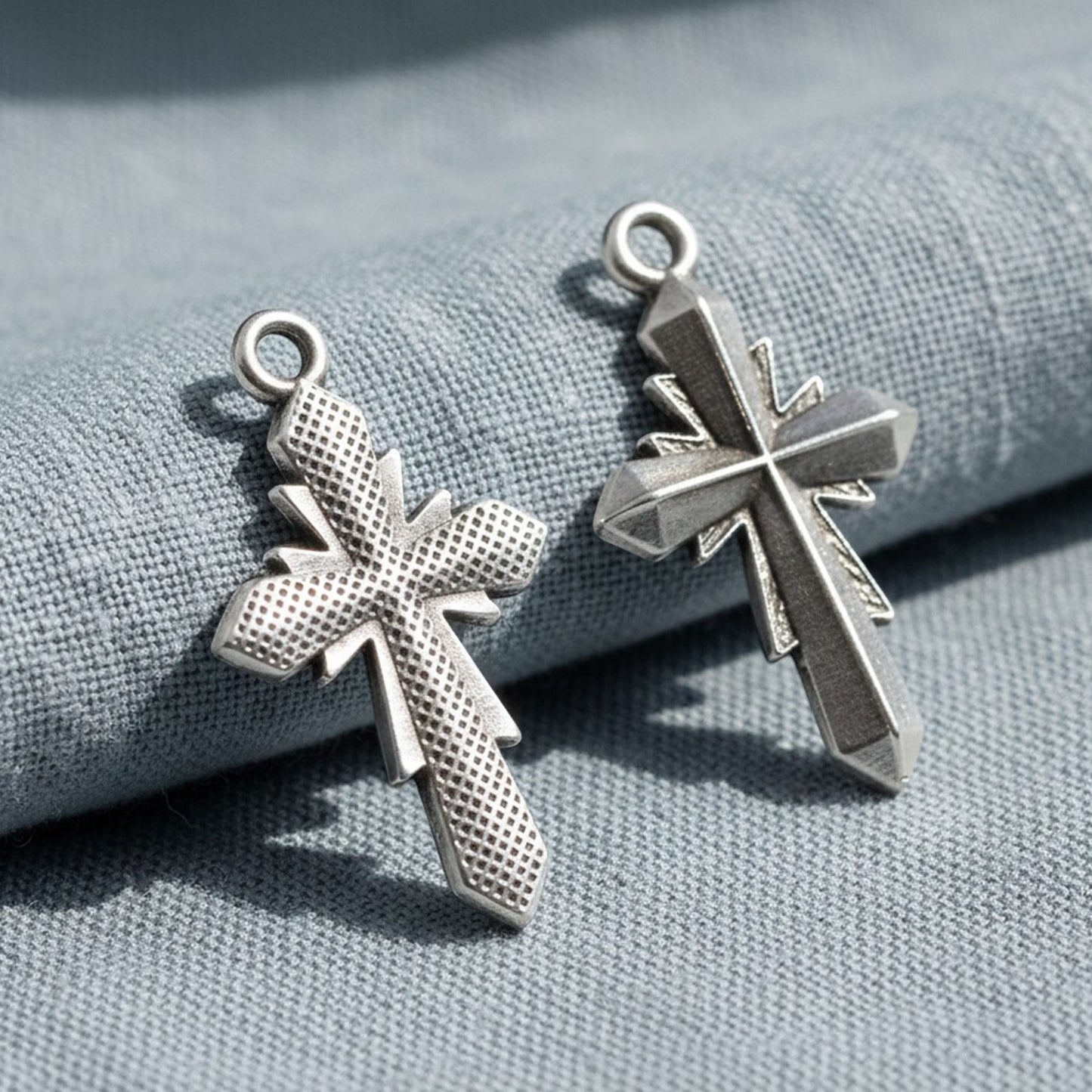 Hackberry Creek silver plated geometric cross pendants with faceted antique finish on blue fabric background.