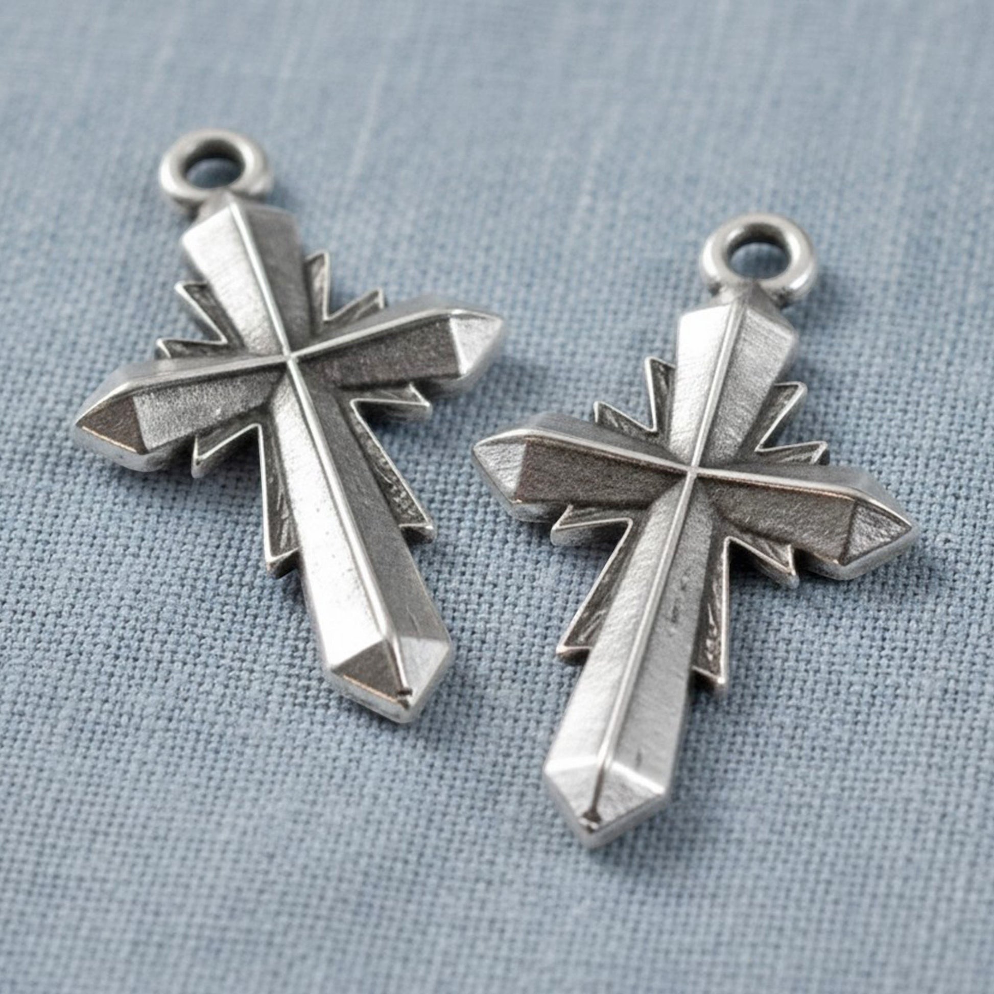 Hackberry Creek silver plated geometric cross pendants with faceted artisan design on a blue fabric background