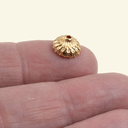 Hackberry Creek 24K gold plated pewter acorn bead cap held on a finger for scale, showing detailed floral texture.