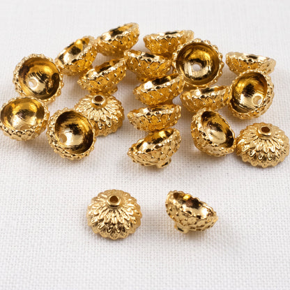 Hackberry Creek 24K gold plated acorn bead caps with detailed texture for jewelry making on a white fabric background.