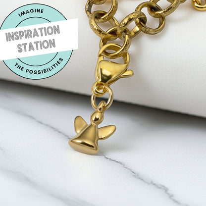 Hackberry Creek 24K gold-plated mini angel charm hanging from a gold chain on a white marble surface.