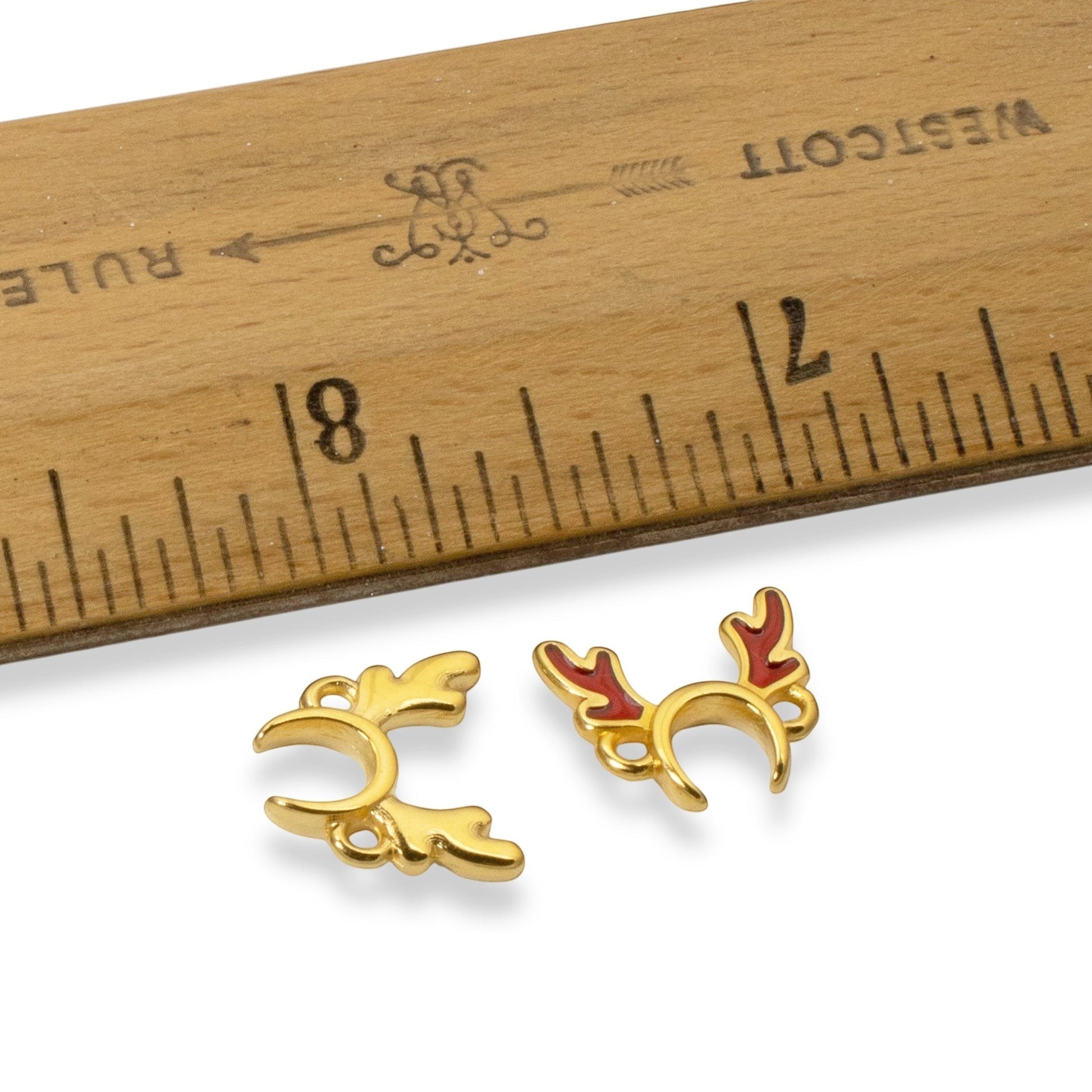 Hackberry Creek 24k gold plated antler jewelry connectors with red enamel details next to a wooden ruler for scale.