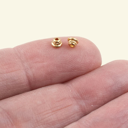 Hackberry Creek 24K gold-plated pewter beaded bead caps for jewelry making, shown on a fingertip for scale.