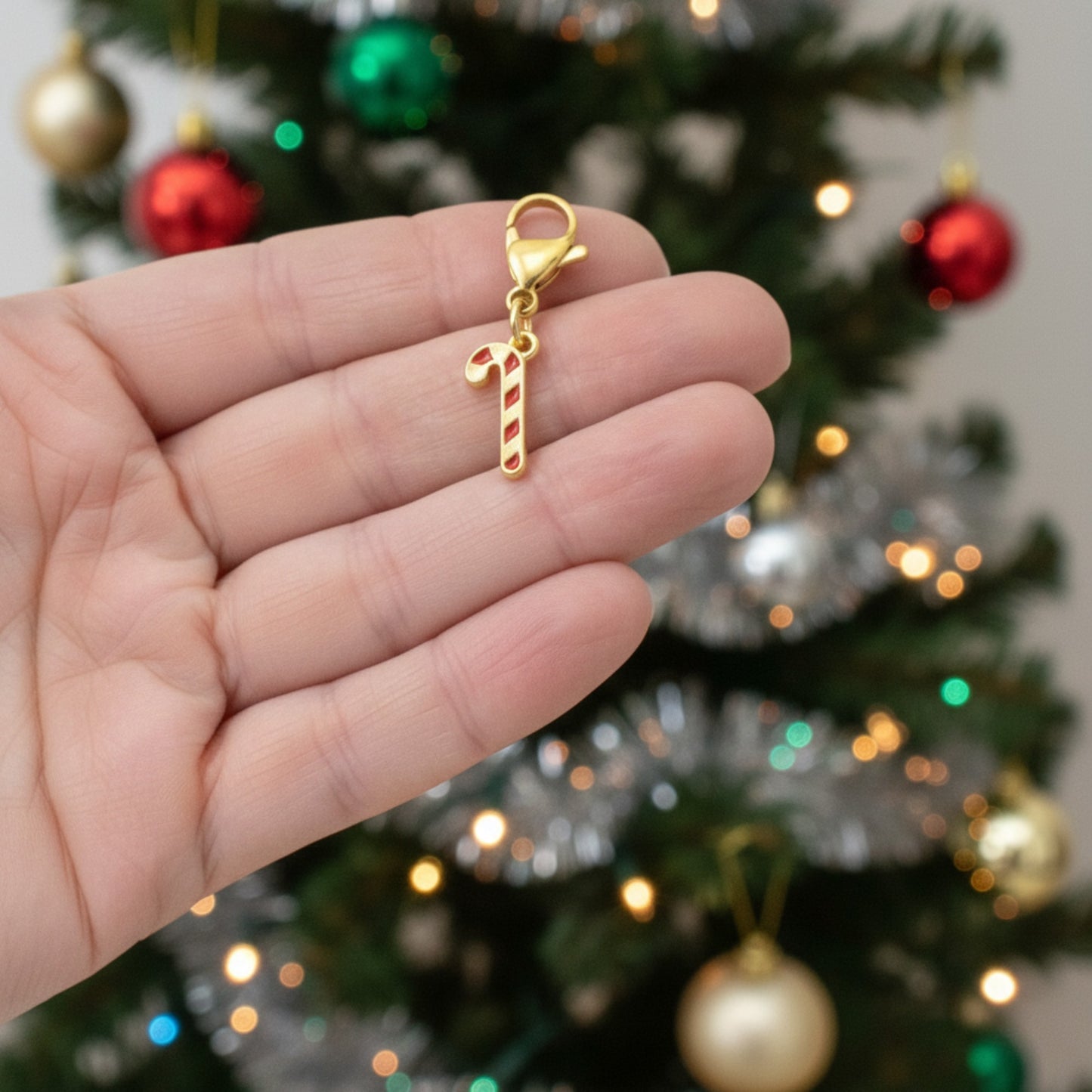 Hackberry Creek 24k gold-plated candy cane charm with red stripes and lobster clasp held against a Christmas tree.