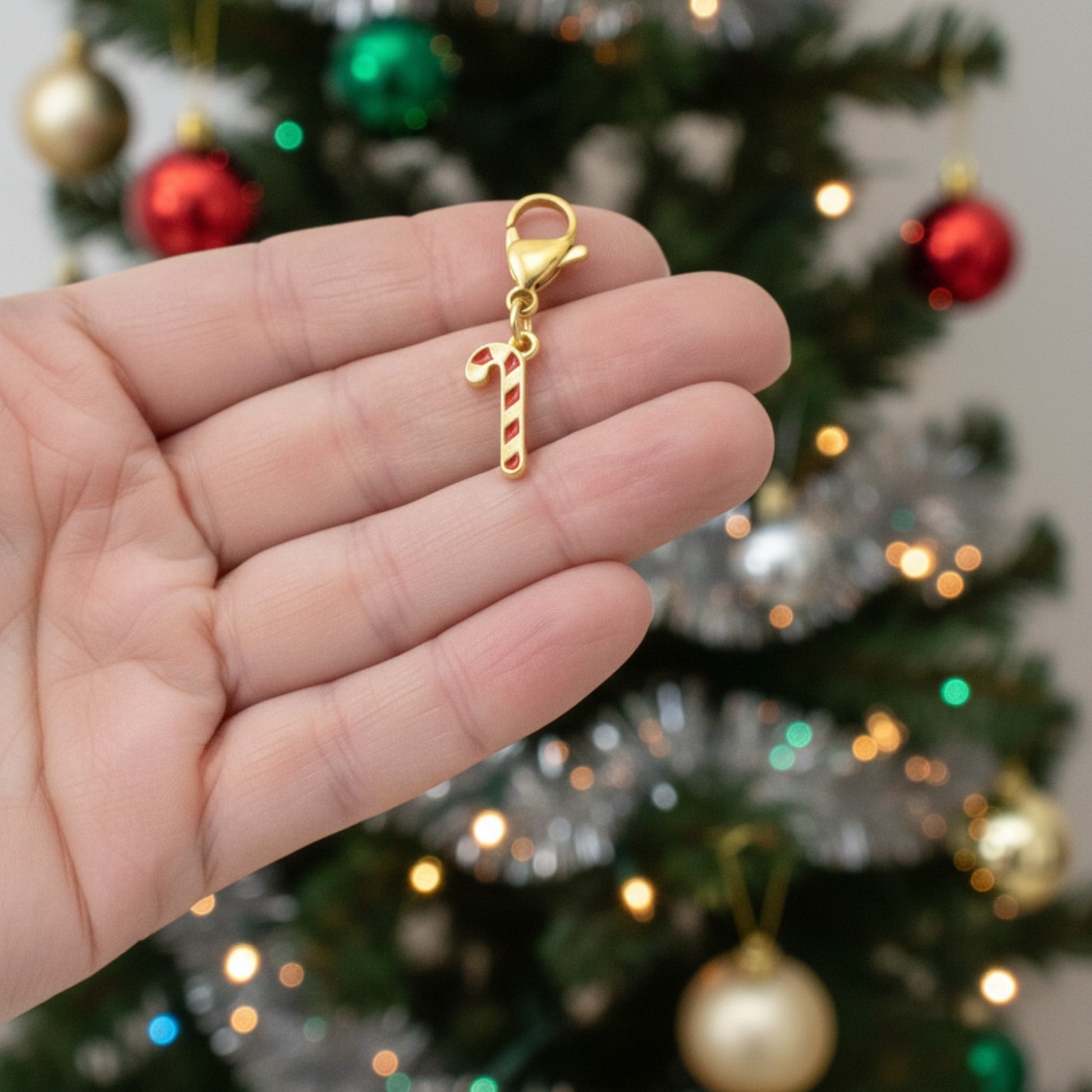 Hackberry Creek 24k gold-plated candy cane charm with red stripes and lobster clasp held against a Christmas tree.