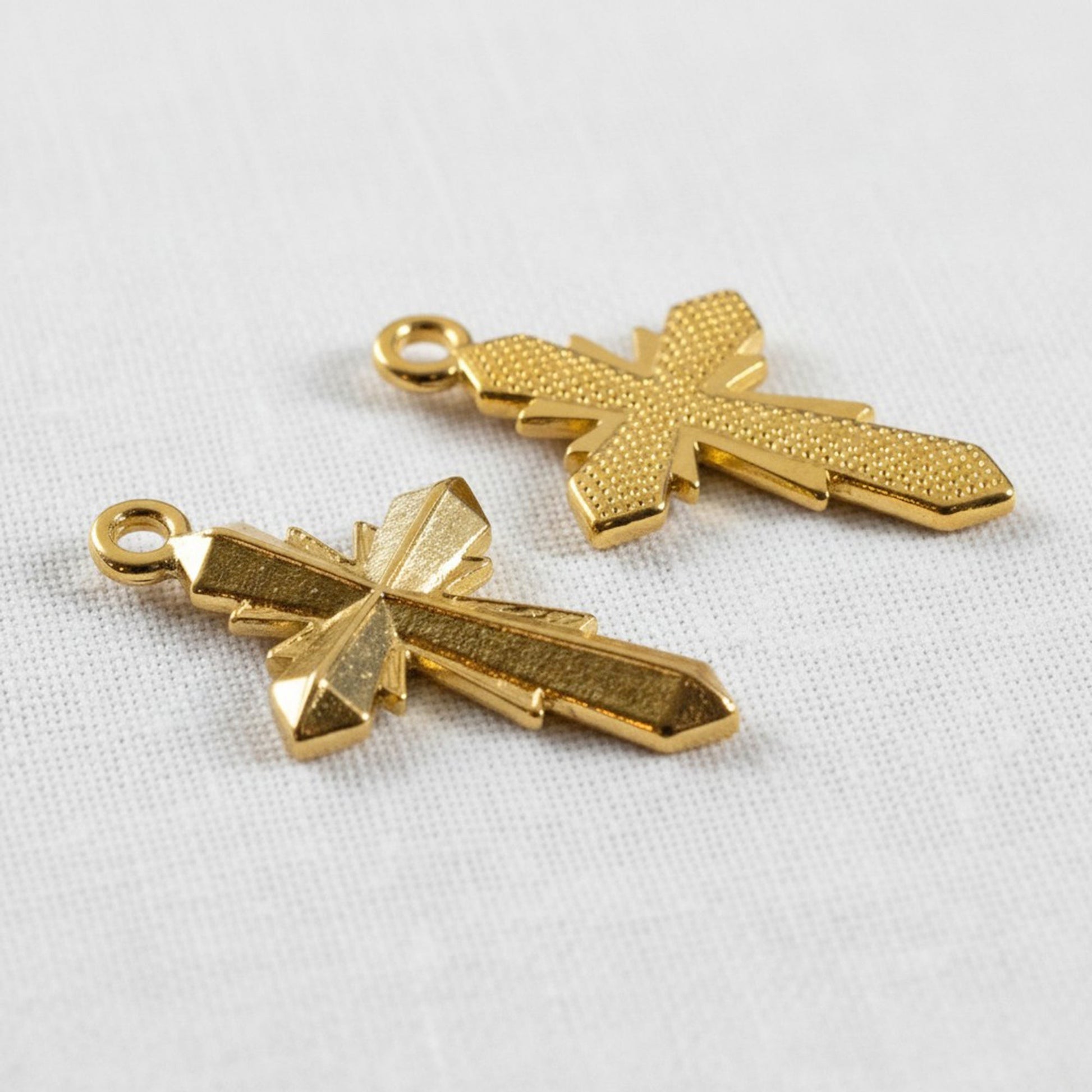 Hackberry Creek two 24K gold plated geometric cross pendants with faceted surfaces and a textured finish.