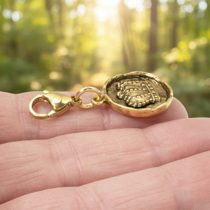 Hackberry Creek antique gold crown charm with a lobster clasp held in a hand against a blurred forest background.