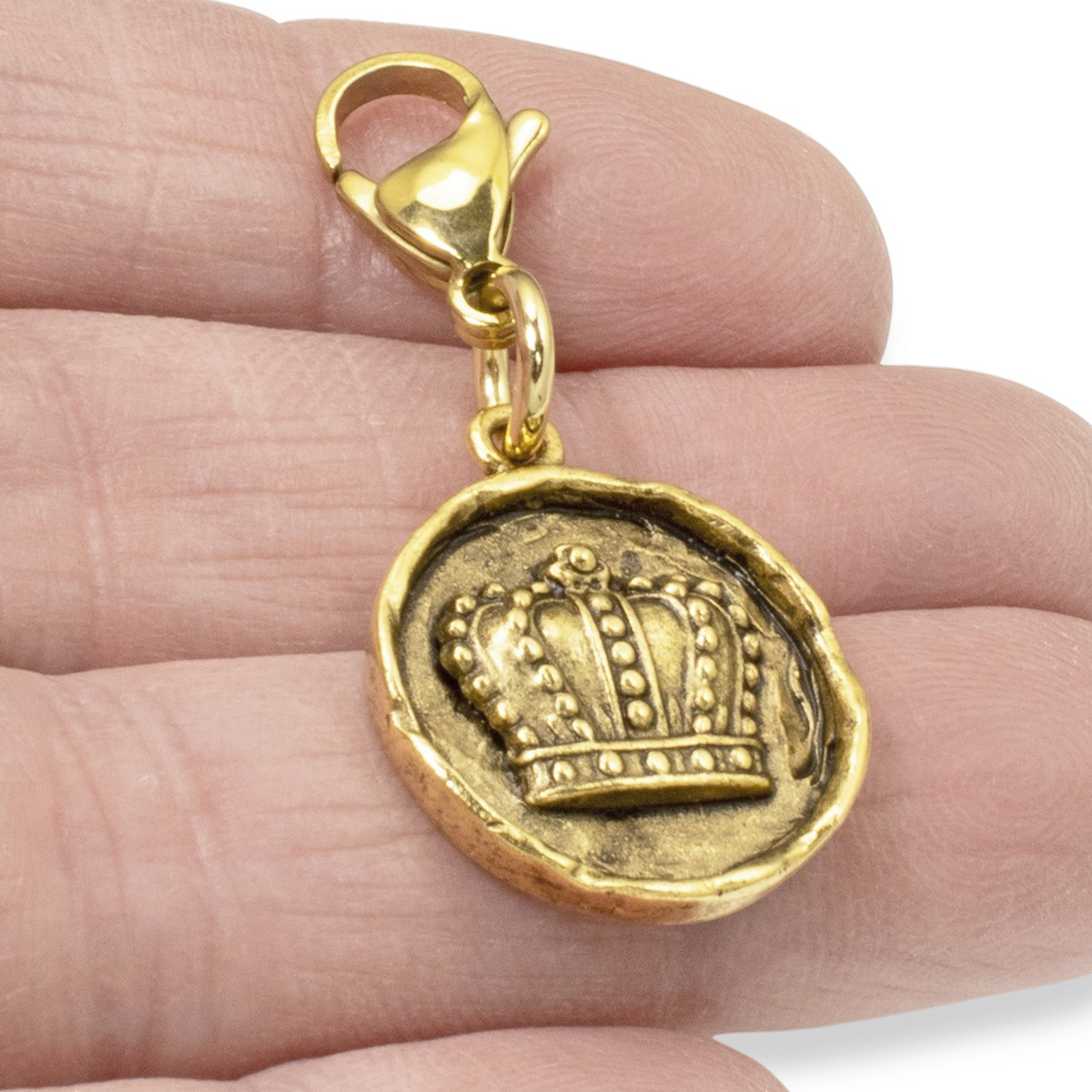 Hackberry Creek gold crown charm with antique finish and lobster clasp held in a hand for scale