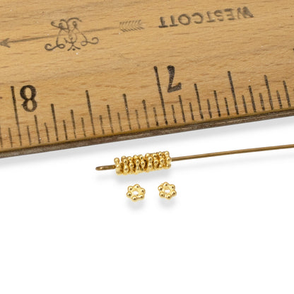 Hackberry Creek 3mm bright gold daisy heishi spacers made of pewter, shown with a ruler for size reference.