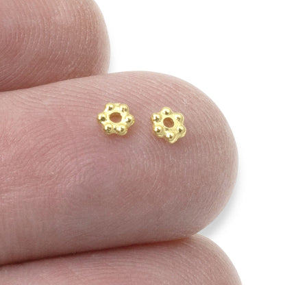 Hackberry Creek 3mm bright gold daisy heishi spacer beads held on a fingertip for scale
