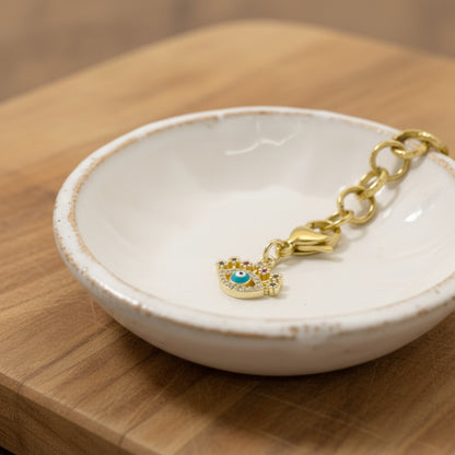 Hackberry Creek gold evil eye charm with blue enamel and CZ accents on a lobster clasp in a small white ceramic dish.