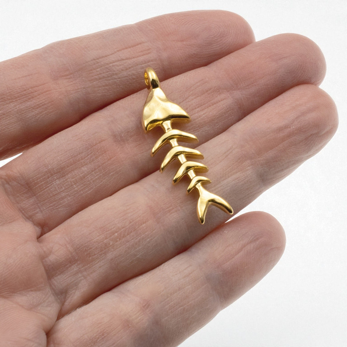 Hackberry Creek 24k gold-plated fishbone skeleton pendant held in a palm for scale, showing detailed coastal design.