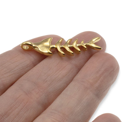 Hackberry Creek gold fishbone skeleton pendant held in hand, featuring detailed 24k gold-plated Zamak coastal design.
