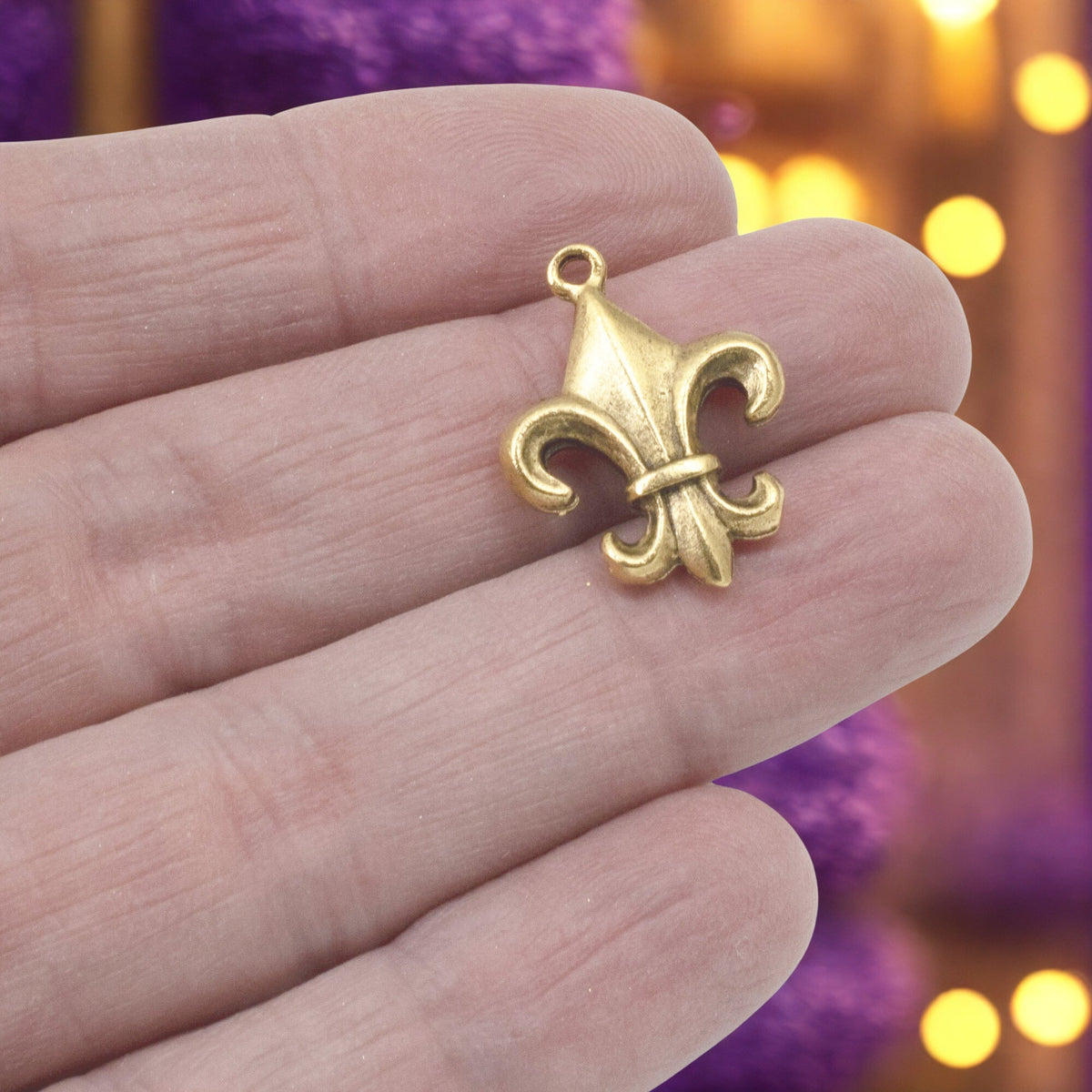 Hackberry Creek gold fleur de lis charm held in hand, featuring an antique finish and intricate French-inspired design.
