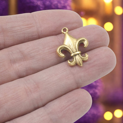 Hackberry Creek gold fleur de lis charm held in hand, featuring an antique finish and intricate French-inspired design.