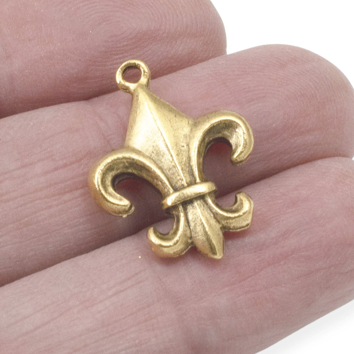 Hackberry Creek gold fleur de lis charm held in fingers, showcasing intricate antique gold plated pewter detail.