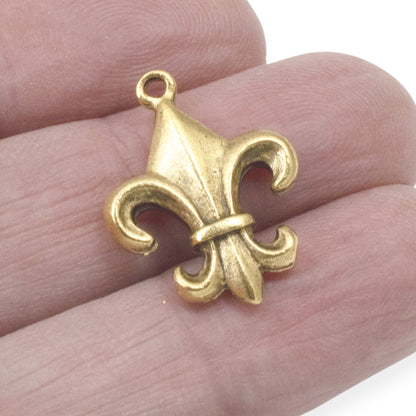 Hackberry Creek gold fleur de lis charm held in fingers, showcasing intricate antique gold plated pewter detail.