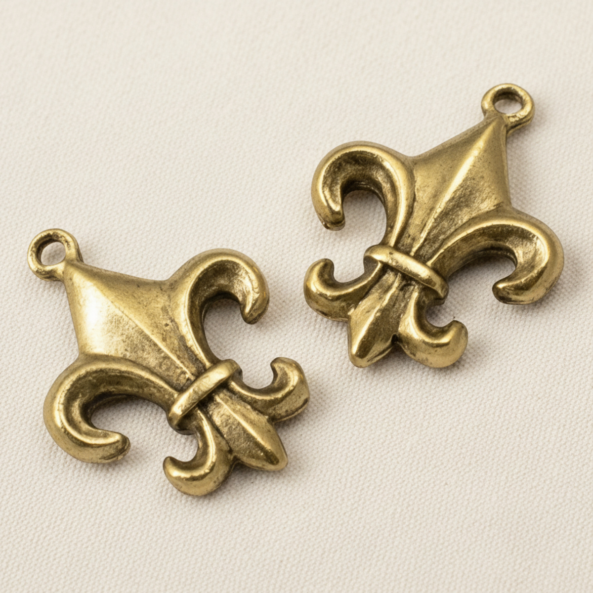 Two Hackberry Creek gold fleur de lis charms with an antique finish and intricate double-sided detailing.