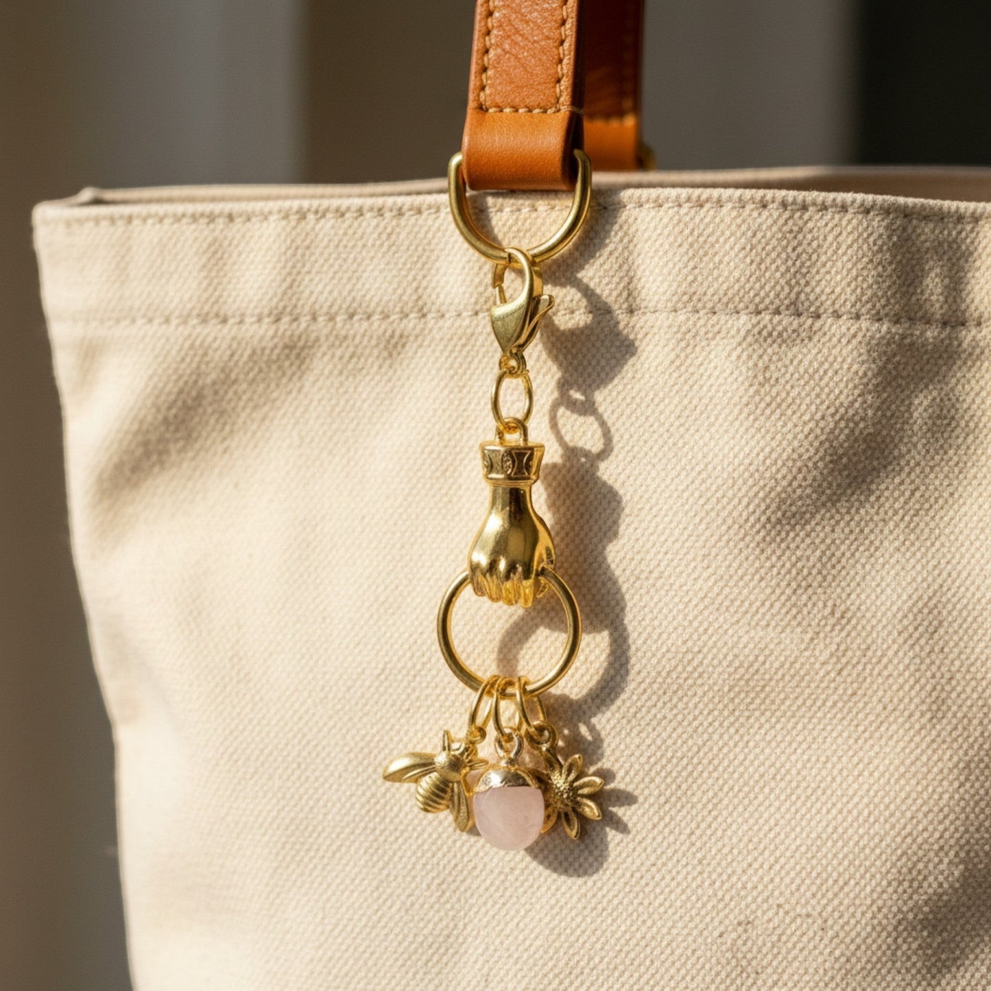 Hackberry Creek gold plated hand charm holder with bee, flower, and rose quartz charms attached to a canvas bag.