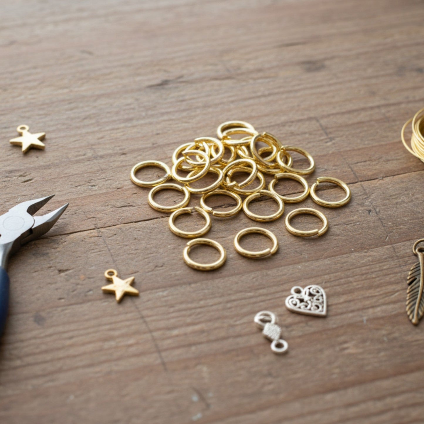 Hackberry Creek 10mm bright gold stainless steel jump rings on a wooden table with jewelry pliers and charms.